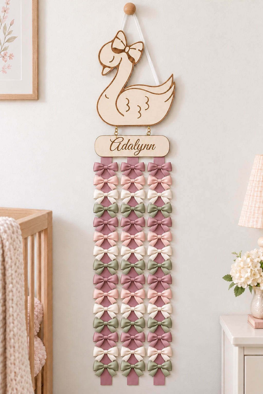 Swan bow holder displaying colorful bows on three mauve ribbon tails