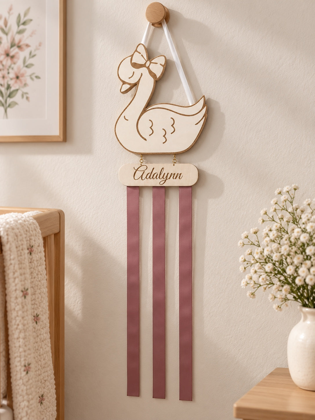Personalized swan bow holder hanging in a softly styled nursery