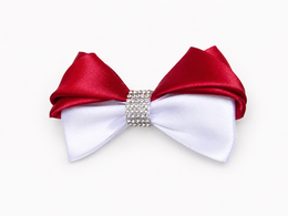 A satin bow accessory with a top half in deep red and a bottom half in white, centered with a sparkling rhinestone band.
