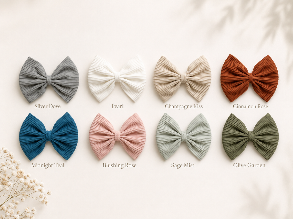 Eight pleated fabric hair bows in muted neutral and pastel colors are arranged in two rows on a light cream background with printed color names beneath each bow. The colors shown are Silver Dove, Pearl, Champagne Kiss, Cinnamon Rose, Midnight Teal, Blushing Rose, Sage Mist, and Olive Garden.
