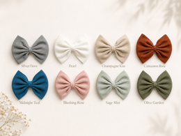 Eight pleated fabric hair bows in muted neutral and pastel colors are arranged in two rows on a light cream background with printed color names beneath each bow. The colors shown are Silver Dove, Pearl, Champagne Kiss, Cinnamon Rose, Midnight Teal, Blushing Rose, Sage Mist, and Olive Garden.
