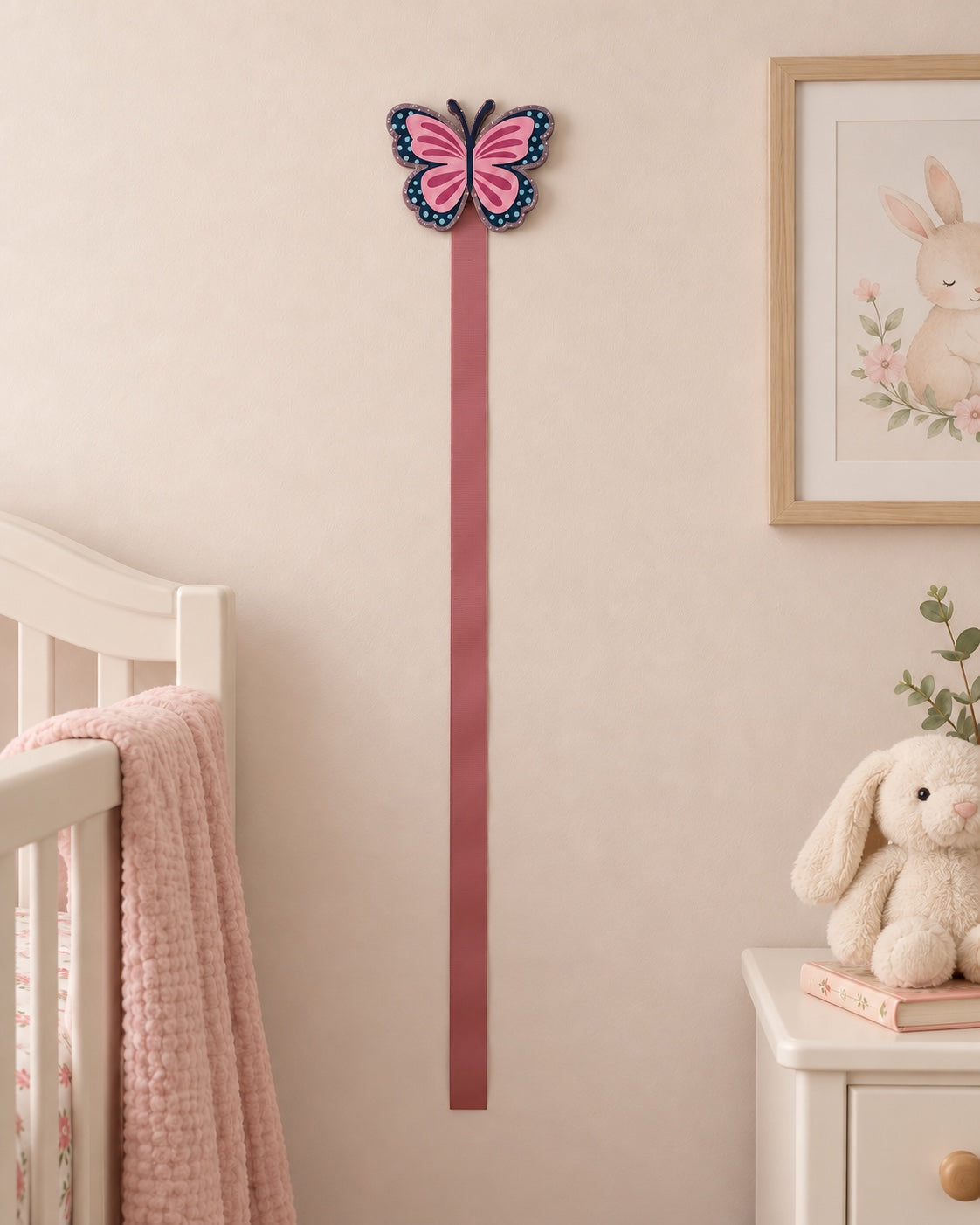 Butterfly bow holder with one pink ribbon displayed on a nursery wall