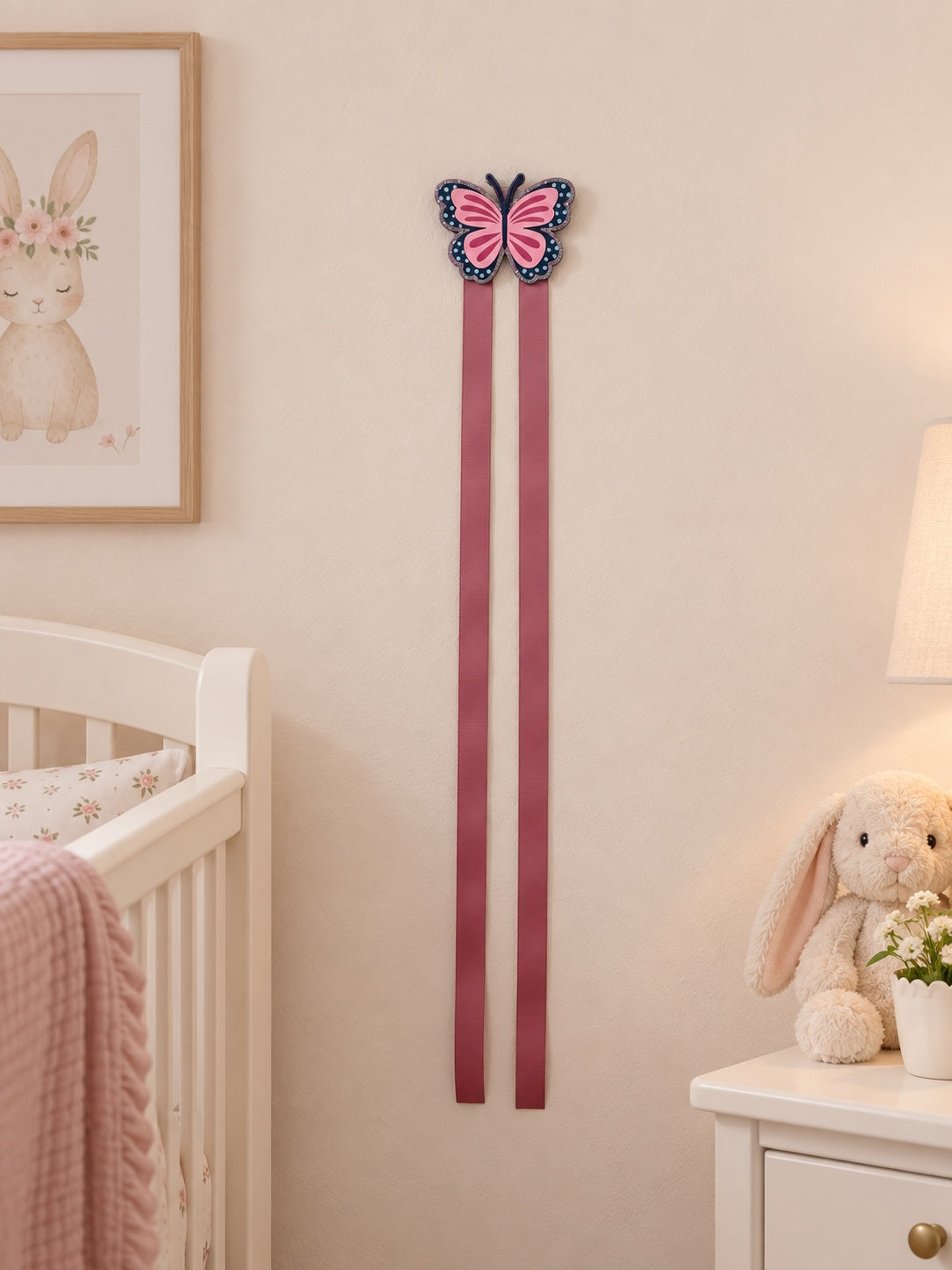 Butterfly bow holder with two pink ribbons displayed on a nursery wall