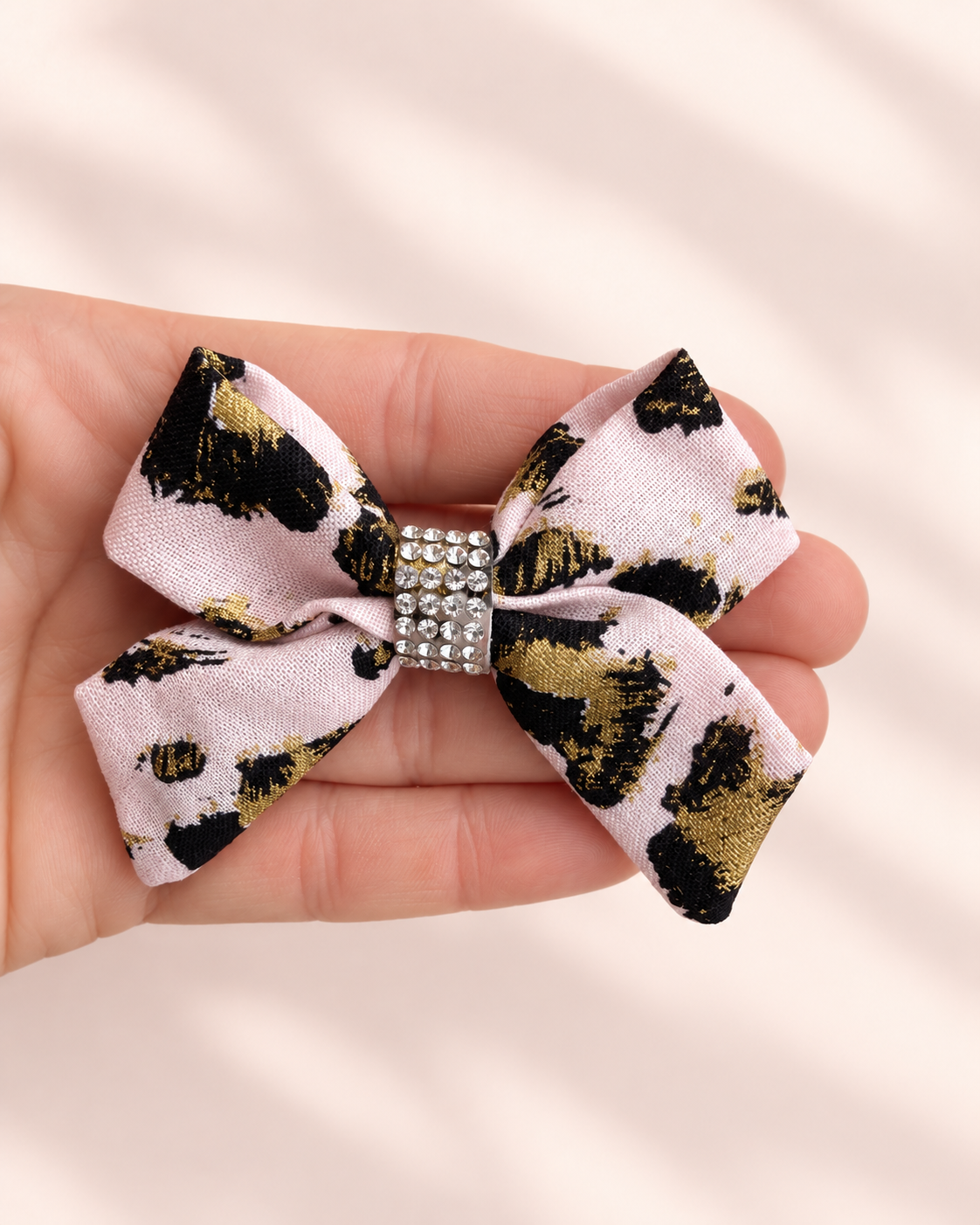 3 inch Gilded Leopard mini hair bow shown in hand for size with blush pink black gold fabric and rhinestone center