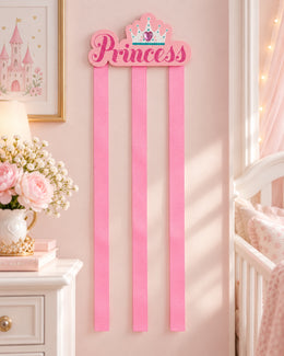 Princess hair bow holder displayed on nursery wall with three pink ribbons