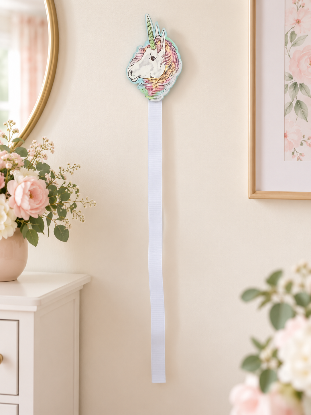 Pastel unicorn bow holder with white ribbon displayed on a soft ivory nursery wall